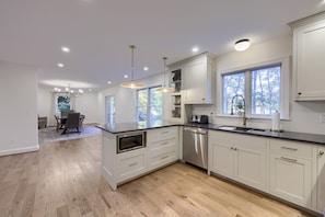 A modern kitchen with white cabinetry, a built-in oven, a dishwasher, and a large window providing natural light.