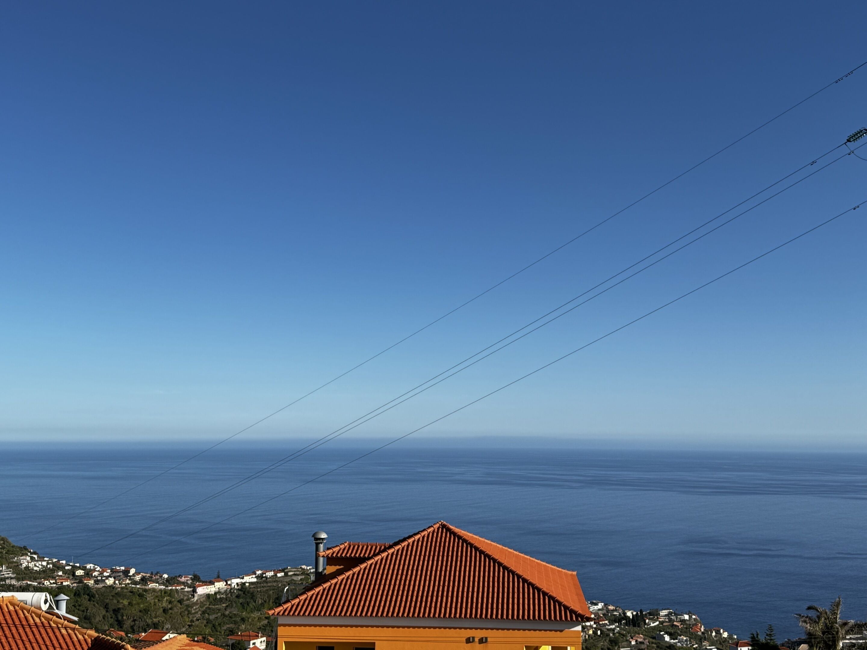 A coastal view with a building featuring a red-tiled roof and a clear blue sky.