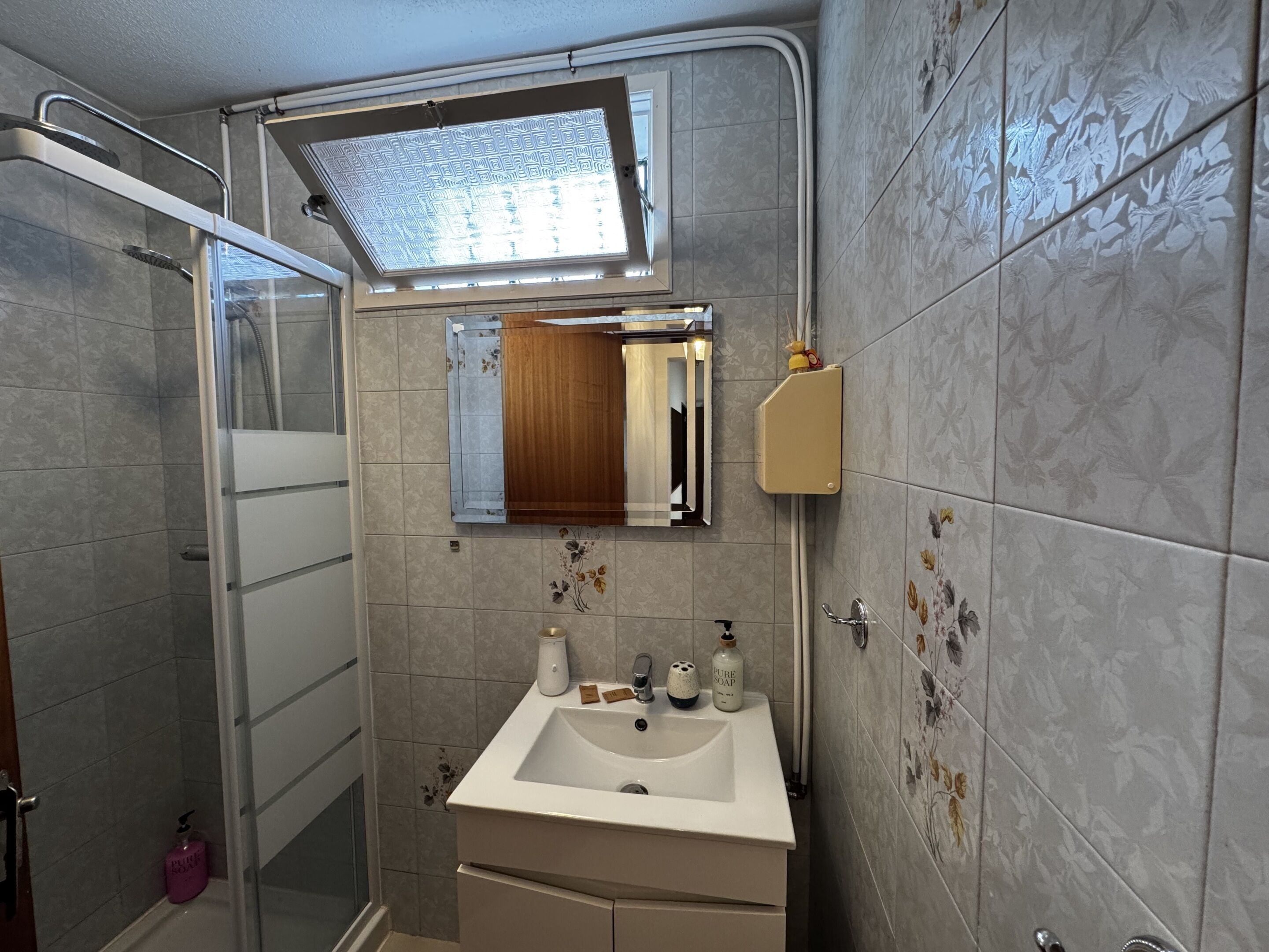 A bathroom with a shower, a sink, a mirror, and a window.