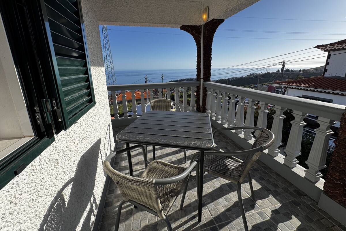 A balcony with a table and chairs, overlooking a coastal view.