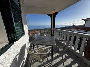 A balcony with a table and chairs, overlooking a coastal view. - Sunrise Villa (Ponta do Sol)