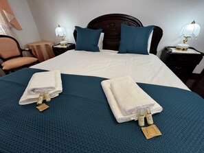 A hotel room with a large bed, two pillows, two nightstands with lamps, a chair, and towels on the bed. - Sunrise Villa (Ponta do Sol)