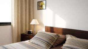 Een hotelkamer met een bed, nachtkastje met lamp, een ingelijste foto aan de muur en een raam met gordijnen.