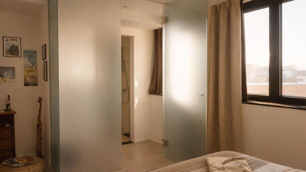 Een slaapkamer met een bed, een raam met gordijnen, een deur naar een badkamer en een muur met ingelijste foto's.