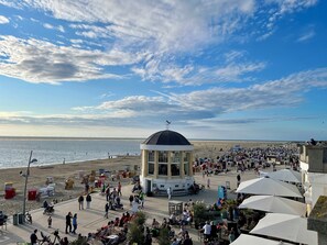 A beachside promenade with a central kiosk, outdoor seating, and umbrellas.