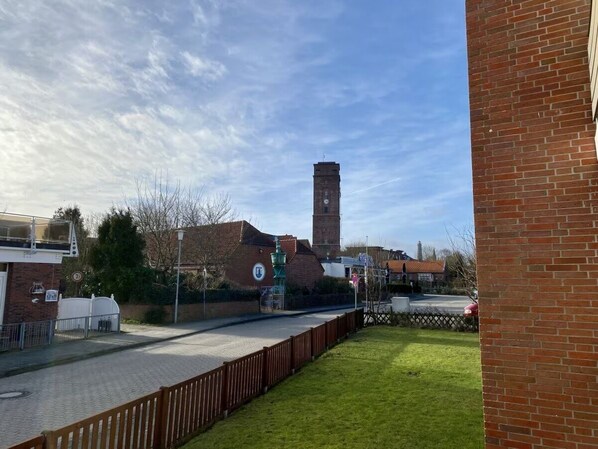 A brick building with a tower, a paved area, and a grassy lawn.
