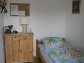 A bedroom with a wooden cabinet, a bed with floral bedding, a lamp, and a bulletin board with papers.