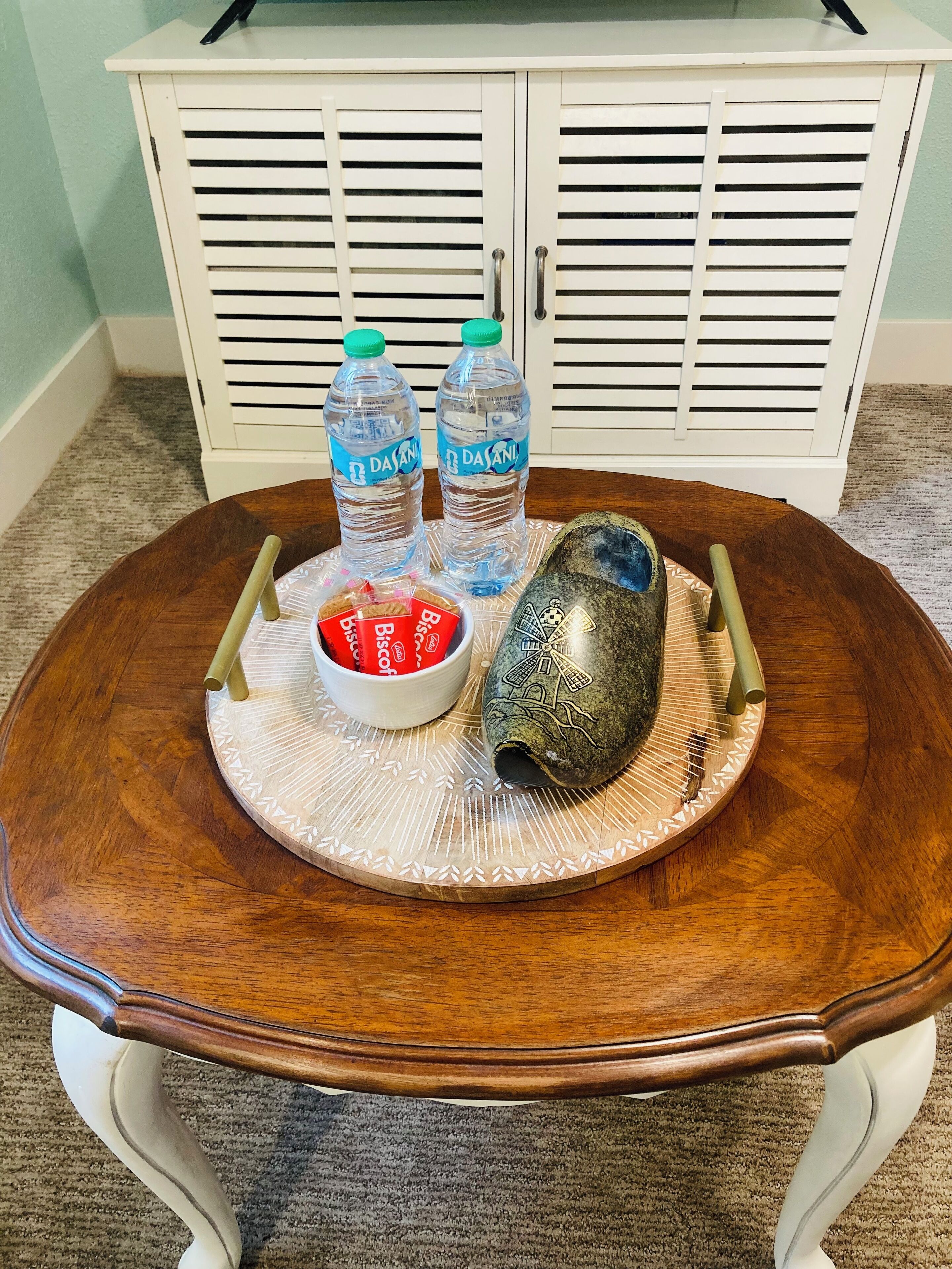 A wooden table with a woven placemat, two Dasani water bottles, a bowl of biscuits, and a decorative stone.