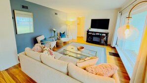 A living room with a sofa, coffee table, and a flat-screen TV. - Summer Retreat in Traverse City: Steps to TART Trail & State Park Beach (Traverse City)