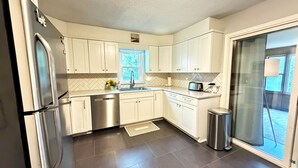 A modern kitchen with white cabinets, stainless steel appliances, a window, and a sliding glass door. - Summer Retreat in Traverse City: Steps to TART Trail & State Park Beach (Traverse City)