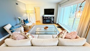 A living room with a sofa, a coffee table, a TV, and a fireplace. - Summer Retreat in Traverse City: Steps to TART Trail & State Park Beach (Traverse City)