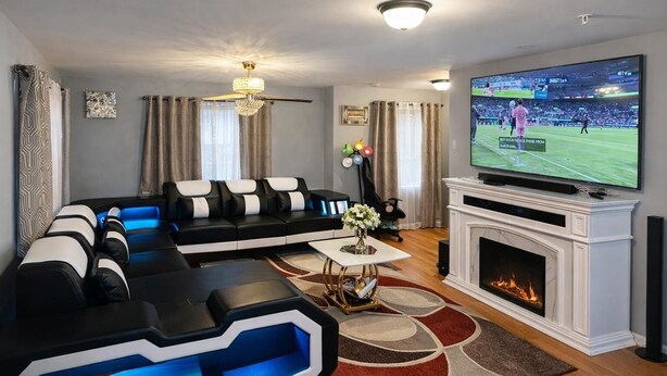 Ein modernes Wohnzimmer mit einem schwarz-weißen Ecksofa, einem Flachbildfernseher, einem Kamin und einer dekorativen Vase auf einem Couchtisch.