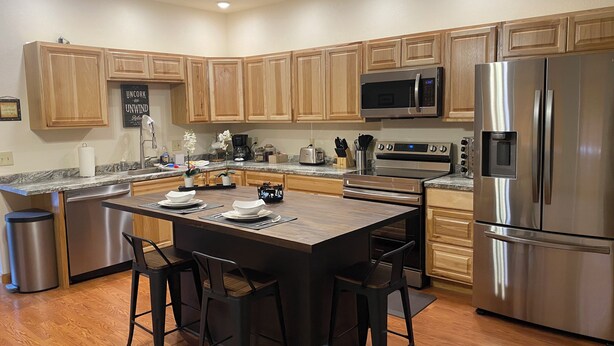 A modern kitchen with wooden cabinets, stainless steel appliances, a central island with bar stools, and a built-in microwave. - Southside 2-bedroom guest suite, ground level with private entrance (Anchorage)