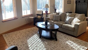 A living room with a sofa, a coffee table, and a lamp. There are windows with blinds, a plant, and a picture on the wall. - Southside 2-bedroom guest suite, ground level with private entrance (Anchorage)