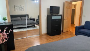 A bedroom with a bed, a dresser, a television, and a blue chair. - Southside 2-bedroom guest suite, ground level with private entrance (Anchorage)