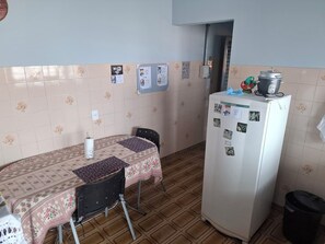 A small kitchen with a table, chairs, a refrigerator, and a trash bin.
