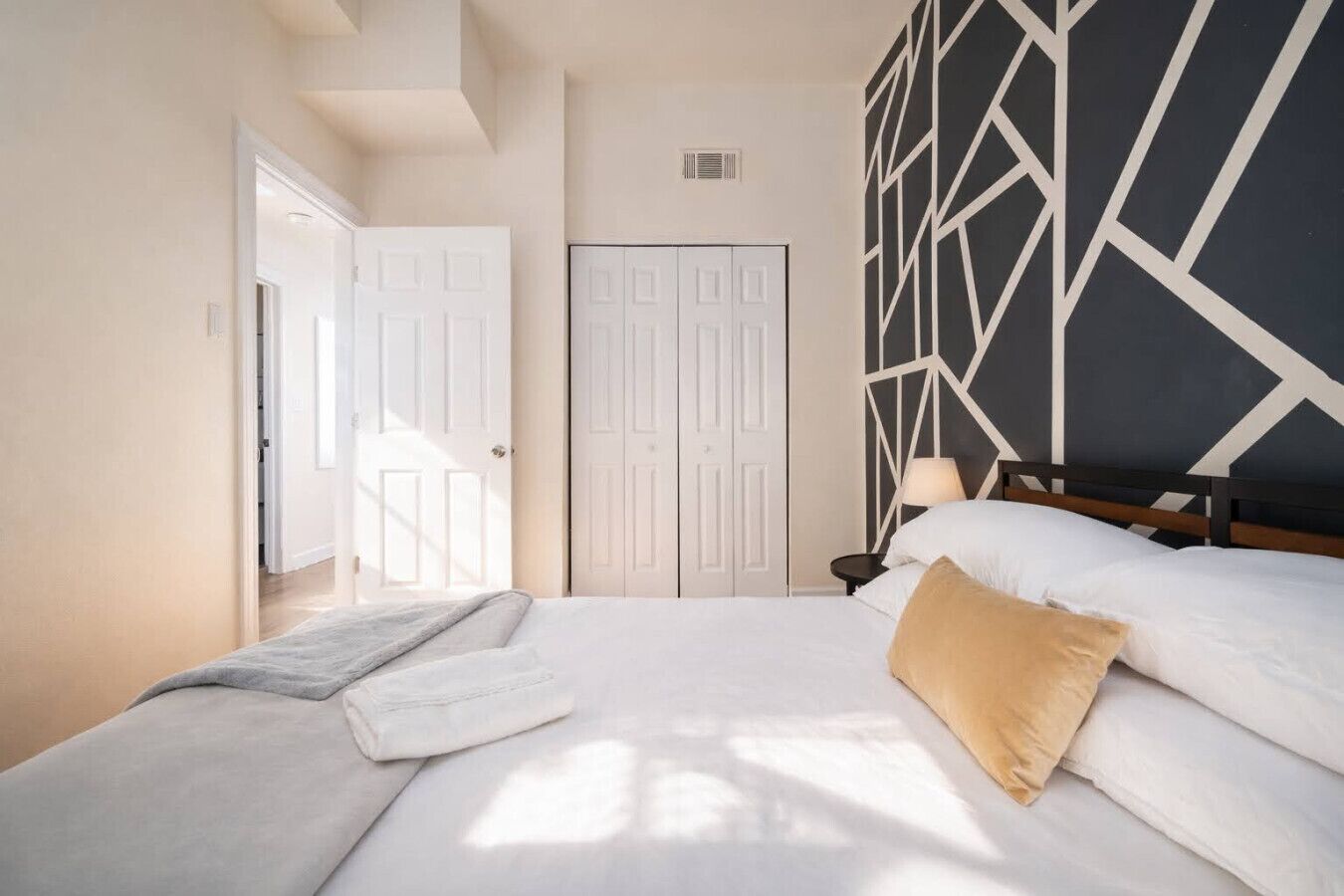 A bedroom with a bed, a nightstand, a lamp, and a geometric-patterned wall.