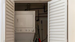 A compact laundry room with a washer and dryer, a vacuum cleaner, and visible plumbing. - Flexhome Ukrainian Village • 2BR • Walkable + Private Balcony (Chicago)