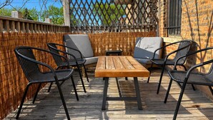A wooden deck with a table and four chairs, surrounded by a bamboo fence. - Flexhome Ukrainian Village • 2BR • Walkable + Private Balcony (Chicago)