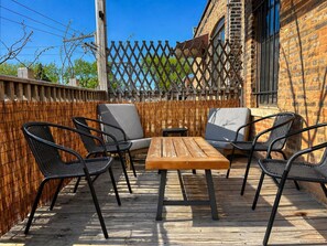 A wooden deck with a table and four chairs, surrounded by a bamboo fence. - Flexhome Ukrainian Village • 2BR • Walkable + Private Balcony (Chicago)