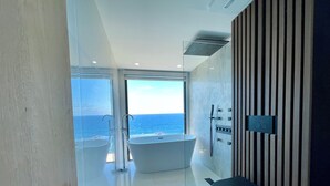 Un bagno moderno con vasca, WC e zona doccia, con una grande finestra vista oceano.