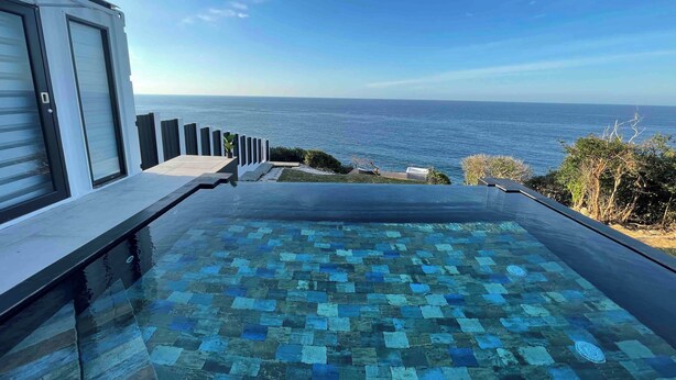 Una piscina a sfioro moderna con un motivo a mosaico, affacciata su un oceano blu e limpido.
