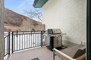 An outdoor patio with a grill, a cushioned seating area, and a view of a hilly landscape.
