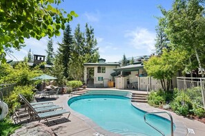 A swimming pool with lounge chairs, a small building, and surrounding greenery. - Townhome across the street from Base Village! (Snowmass Village)