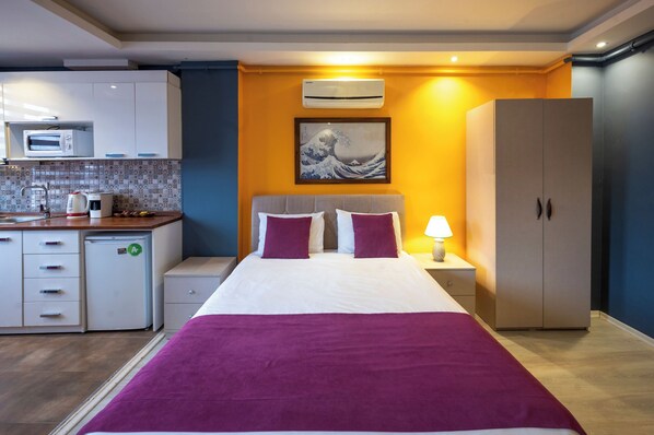 Ein Hotelzimmer mit Bett, Nachttisch, Lampe, Kleiderschrank, Mikrowelle, Kaffeemaschine und kleinem Kühlschrank.