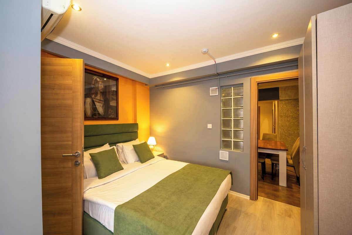 A bedroom with a bed, bedside table, lamp, and a view of a dining area.