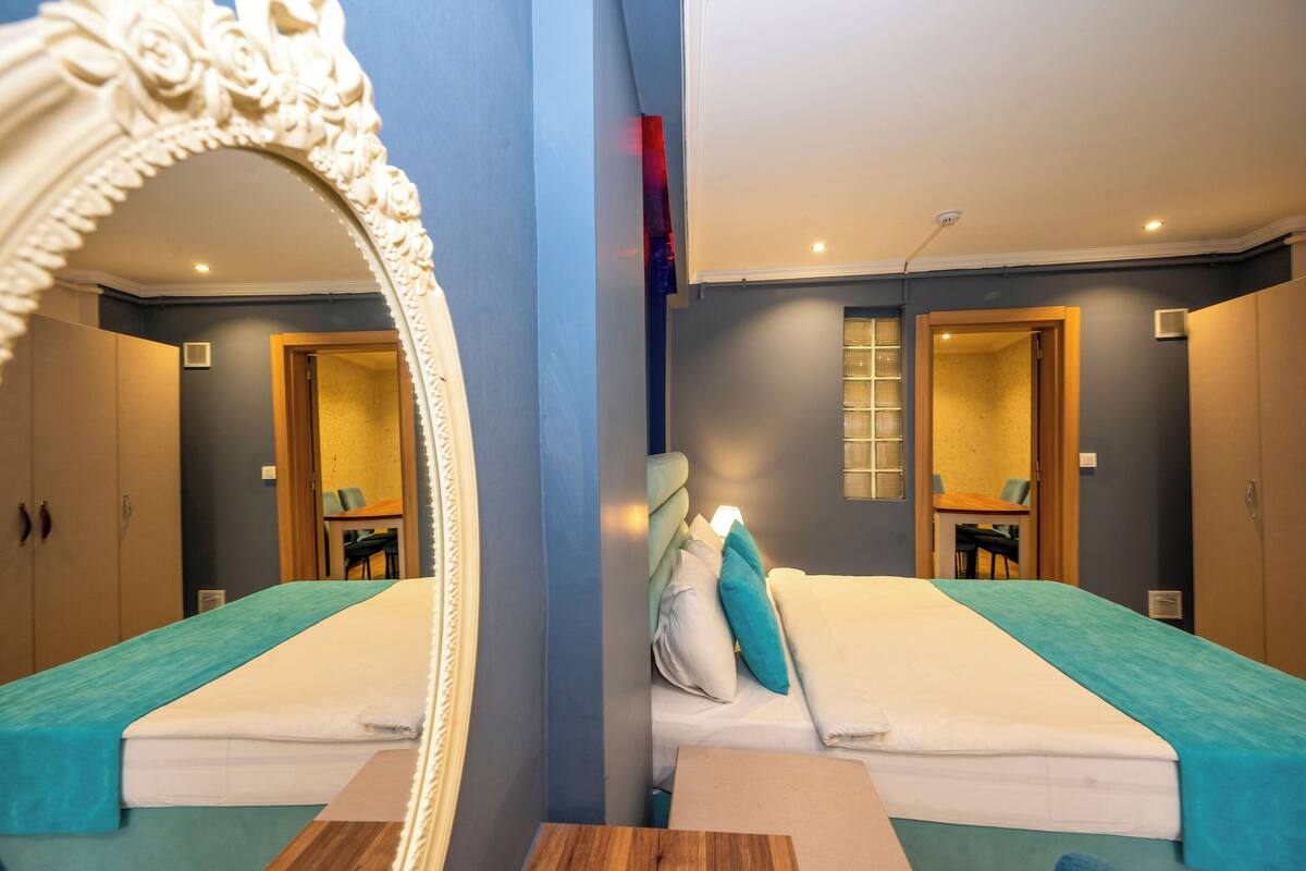 A mirrored room with two beds, a wooden table, and a mirror with an ornate frame.