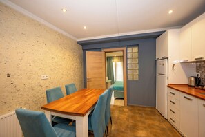 Eine kleine Küche mit Holztisch und blauen Stühlen, einem Kühlschrank und einem Fenster mit Vorhängen.