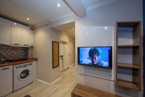 Eine moderne Küche mit eingebauter Waschmaschine, einem flachbildfernseher an der Wand und einem Holzbodenregal.