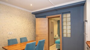 Una stanza con un tavolo da pranzo in legno e sedie blu, un armadio in legno, un bagno piccolo con un asciugamano verde e un frigorifero bianco.
