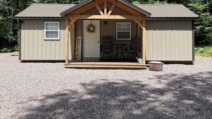 Eine kleine, eingeschossige Holzhütte mit einer Veranda, einer Tür mit einem Kranz und einem kleinen Tisch mit Stühlen.