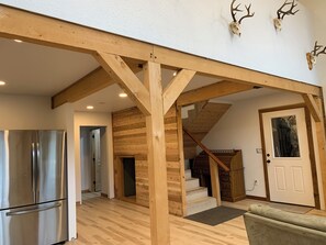 A spacious living area with a wooden ceiling, a staircase, and a door with a window.