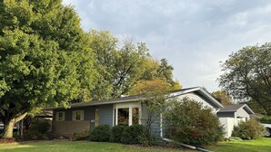 A single-story house with a sloped roof, surrounded by a well-maintained lawn and trees. - Sleeps 10 - 5BR - Minutes to Campus - Next to Park, Golf, Shopping (Ames)