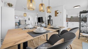 A modern dining area with a wooden table, black chairs, and three pendant lights. - Havhus - Sauna, fireplace, washing machine, electric vehicle charging station (Olpenitz)