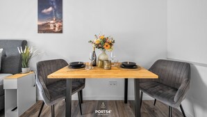 Un coin repas avec une table en bois, deux chaises grises à revêtement rembourré, un vase avec des fleurs et un tableau encadré représentant un paysage urbain.
