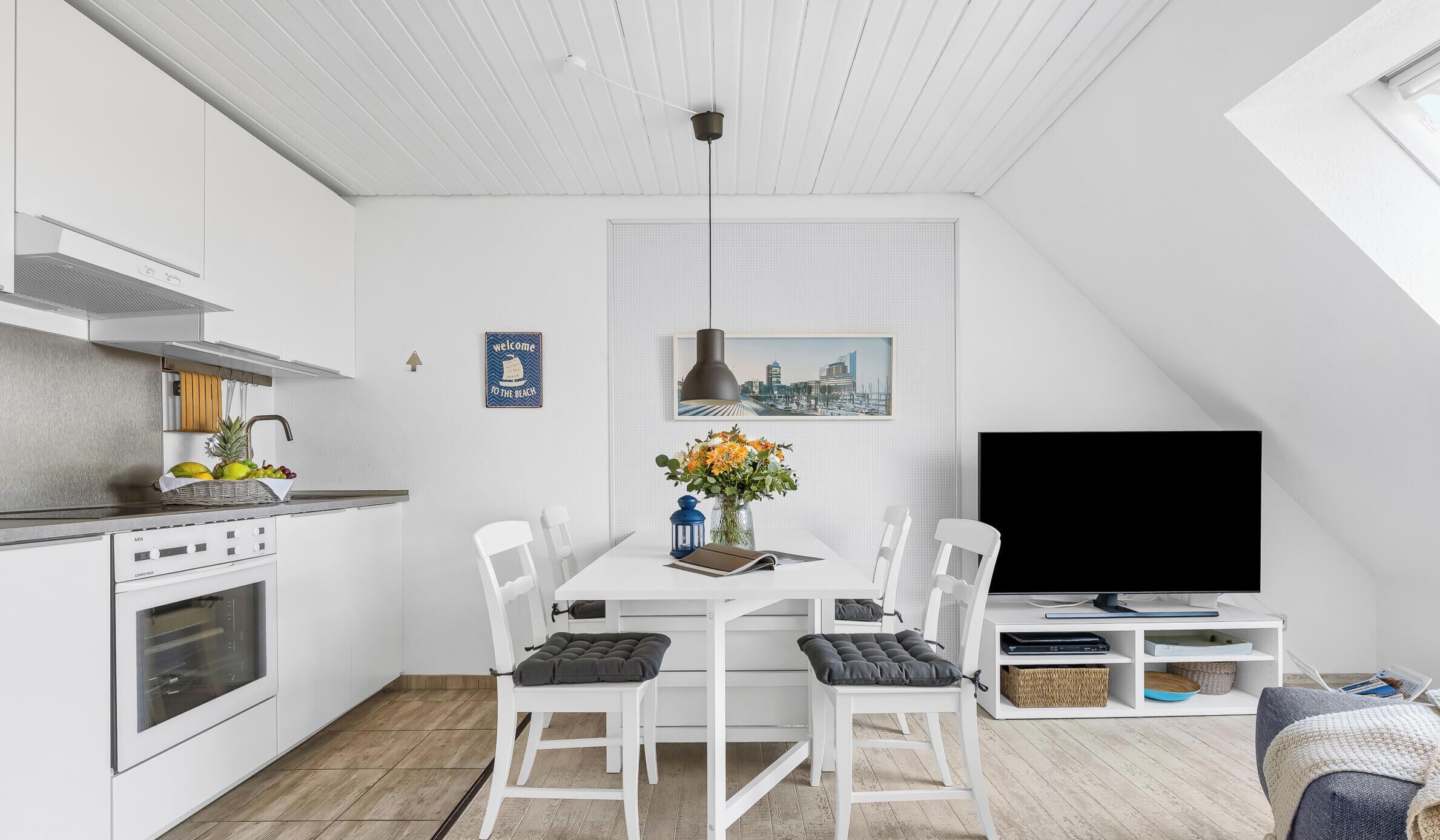 A modern kitchen with white cabinetry, a built-in oven, and a dining area with a white table and chairs.