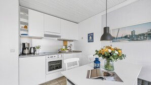 Ett modernt kök med vita köksskåp, en inbyggd ugn och en matplats med ett vitt bord.