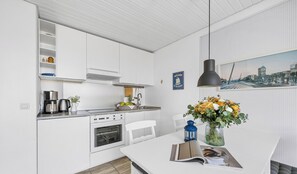 A modern kitchen with white cabinetry, a built-in oven, and a dining area with a white table.