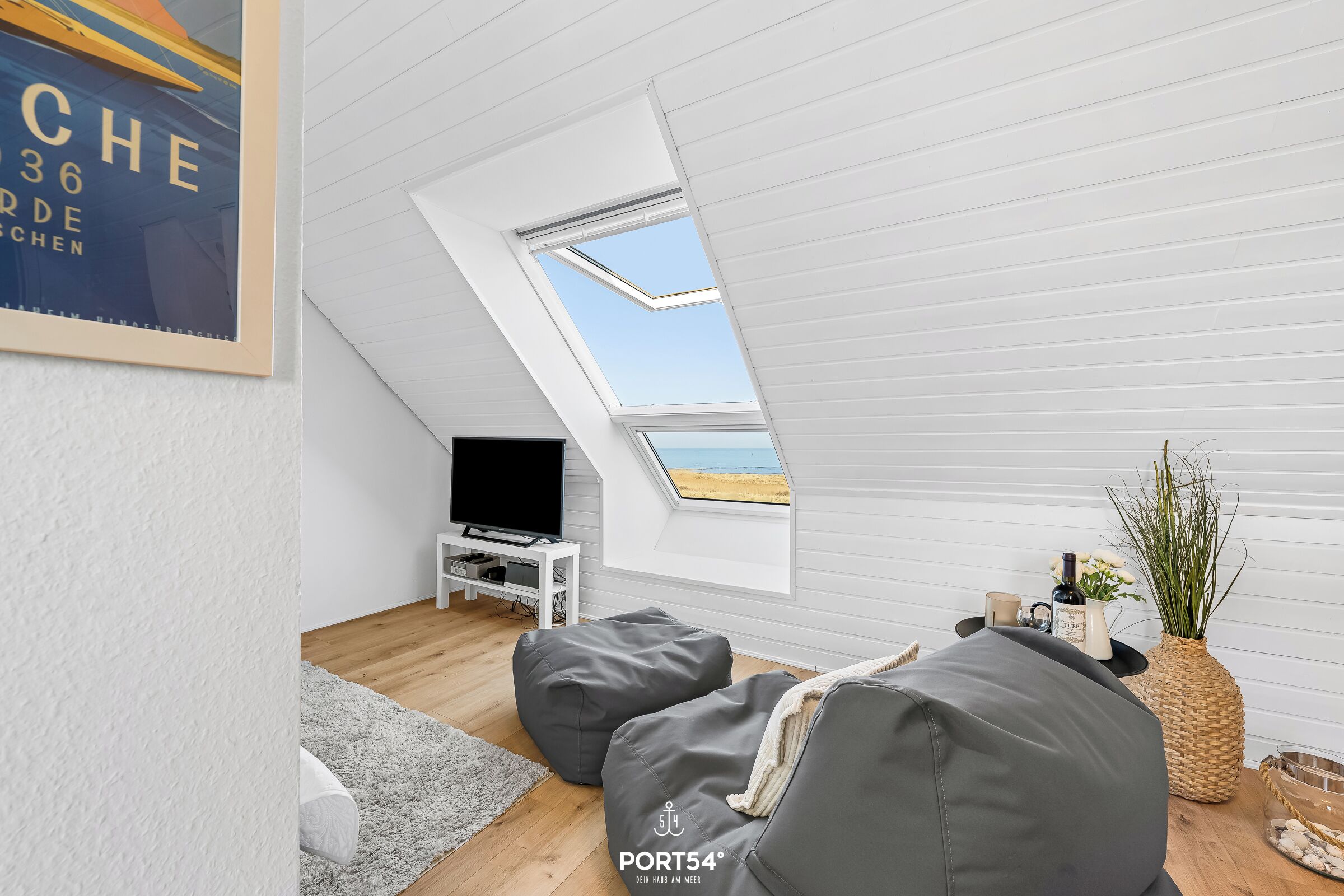 A modern loft bedroom with a skylight, a television, grey bean bag chairs, and a wicker vase on the wooden floor.