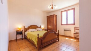 Ein Schlafzimmer mit einem hölzernen Bett, einem Nachttisch, einem Kleiderschrank, einem Heizkörper und einem Fenster.