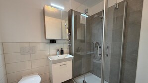 Et moderne badeværelse med en glasafskærmet brusekabine, en hvid vask og et toilet.