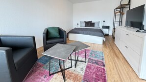 Et moderne soveværelse med seng, lille bord, stol, fjernsyn og kommode.