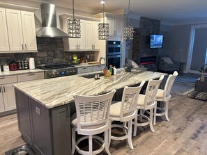 A modern kitchen with a large island, white cabinetry, and a stone backsplash. - Minutes to Acrisure, two balconies with city views, two car garage (Pittsburgh)