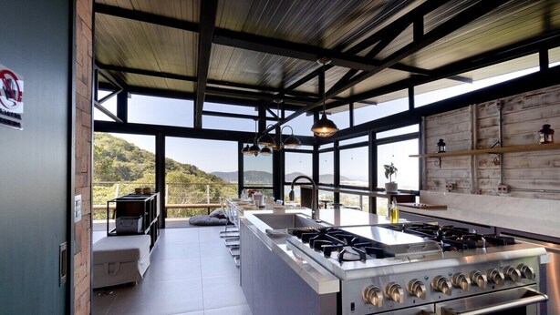 Cozinha moderna com uma ilha grande, eletrodomésticos de aço inoxidável e vista para o exterior.