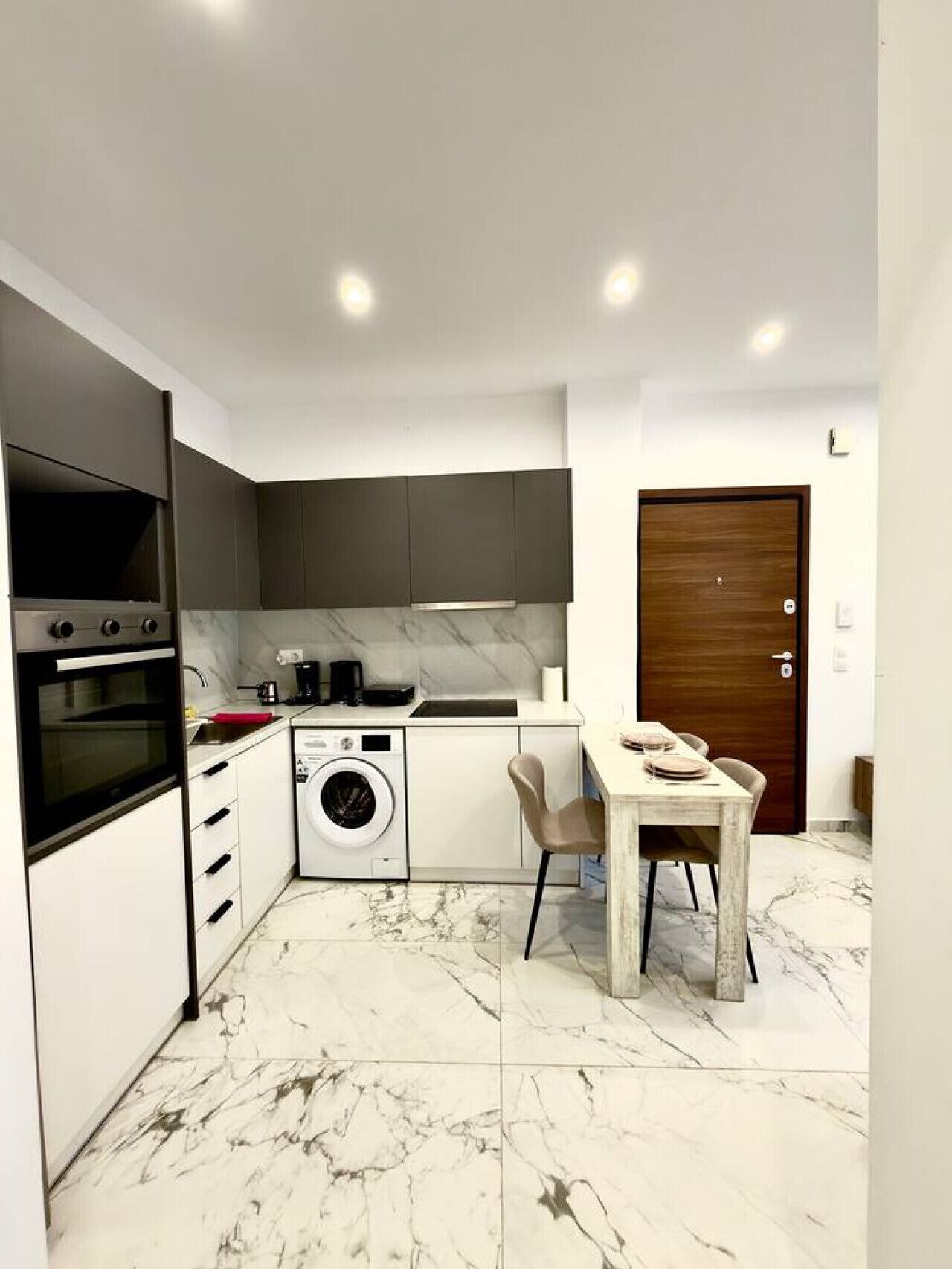 A compact kitchen with a built-in oven, a washing machine, and a dining area with a table and chairs.