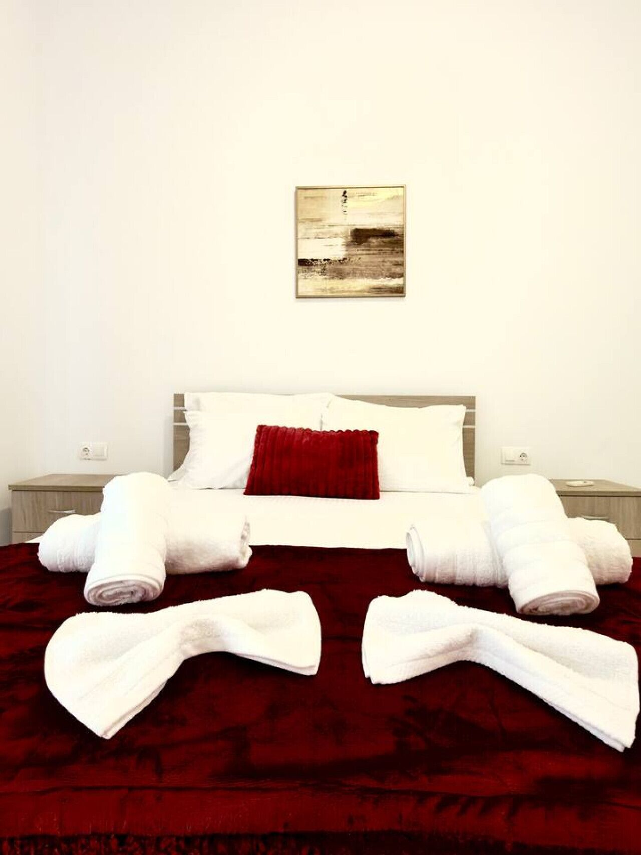 Een hotelkamer met een bed, rode beddengoed, witte kussens, een rood sierkussen en netjes opgevouwen handdoeken op het bed.